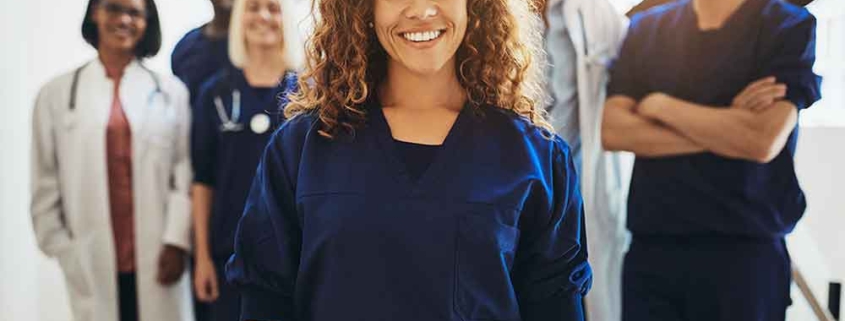 A smiling healthcare worker stands with a team of hospital staff