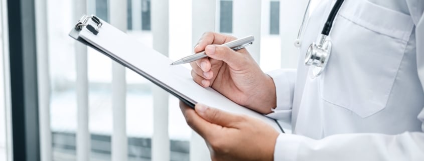 Doctor is standing and reading medical report inside his office